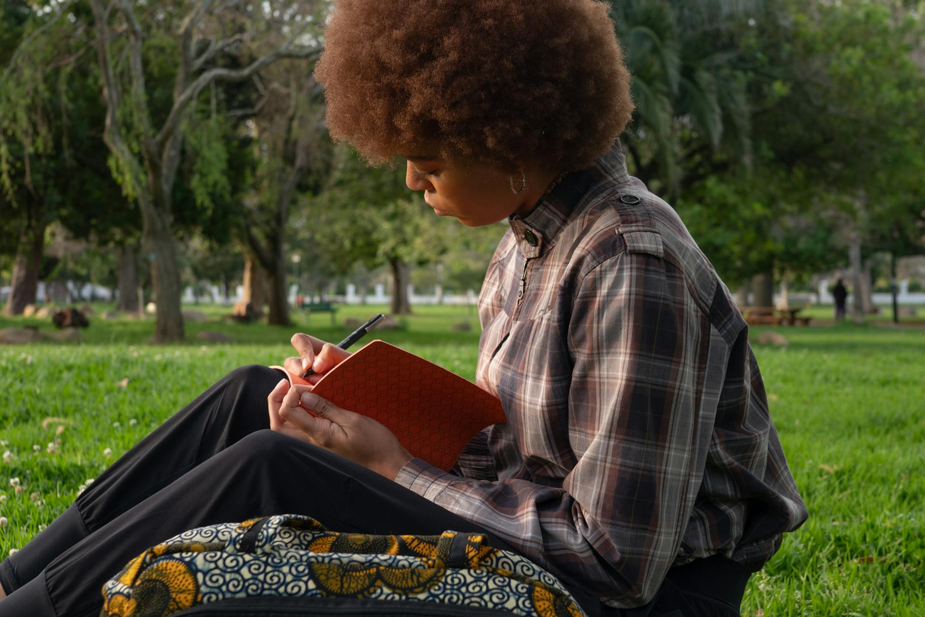 A woman sitting in the grass and writing in a notebook. 